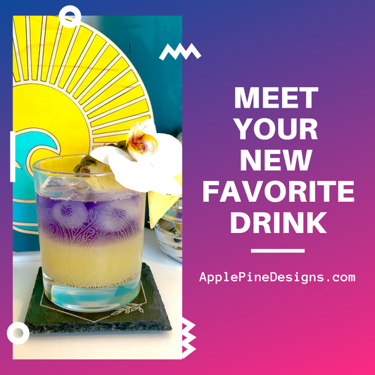 Refreshing Gin cocktail made with pineapple juice and empress gin. Resting on a slate coaster, in an etched glass, and garnished with a flower. Empress gin is purple and layered on top of yellow pineapple juice served over ice.
